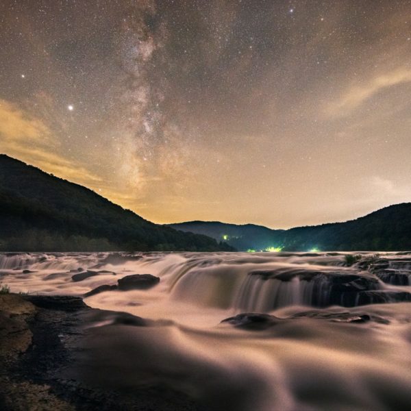 A late summer Milky Way streams above a flowing Sandstone Falls of the New River in West Virginia, appearing to luminesce under the starry night sky.